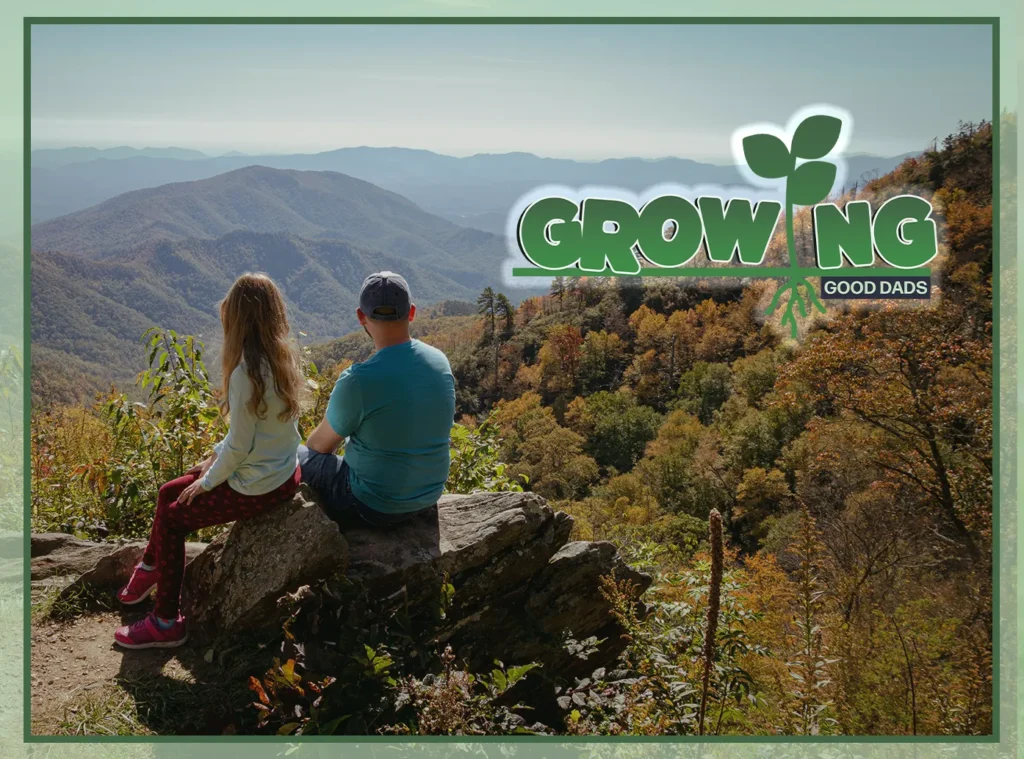 A dad and tween daughter sit on a large rock and look out over a hilly hiking area