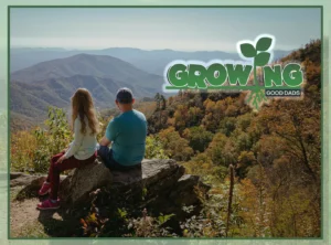 A dad and tween daughter sit on a large rock and look out over a hilly hiking area