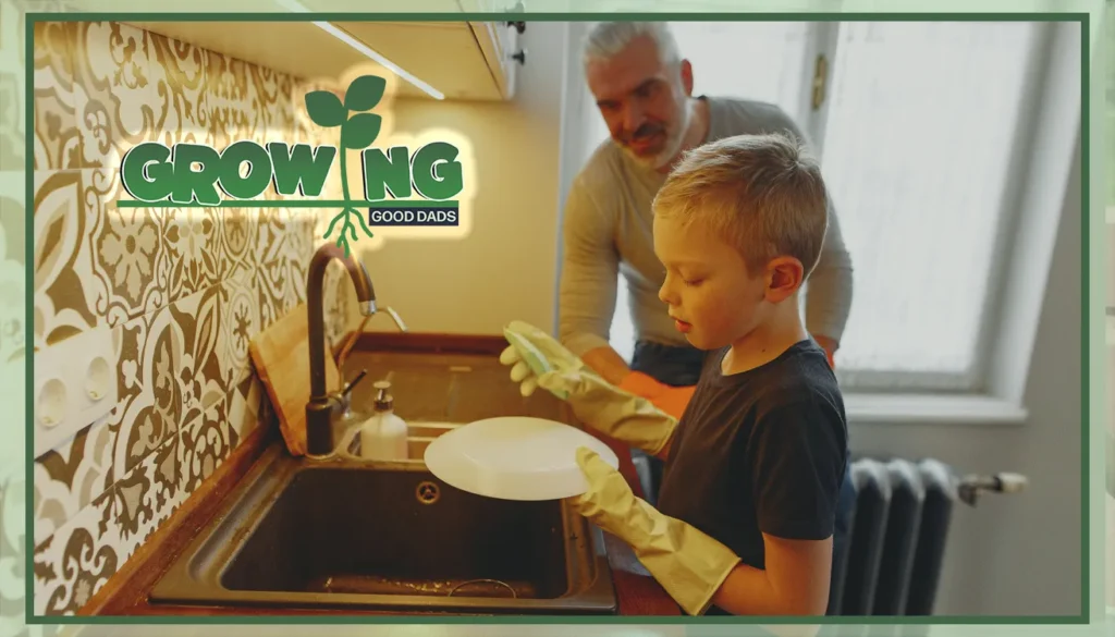 A young blond boy stands at the kitchen sink next to his father while wearing rubber gloves and a dish sponge to wash the dishes.