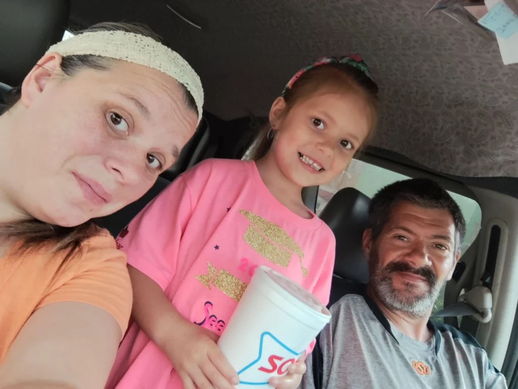 Michael, Mindy and daughter Macy smile for a selfie in a car.