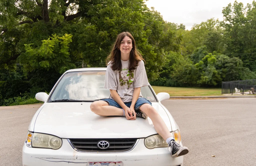 Reagan sits on the hood of the car that she and AJ share as they've learned to drive.