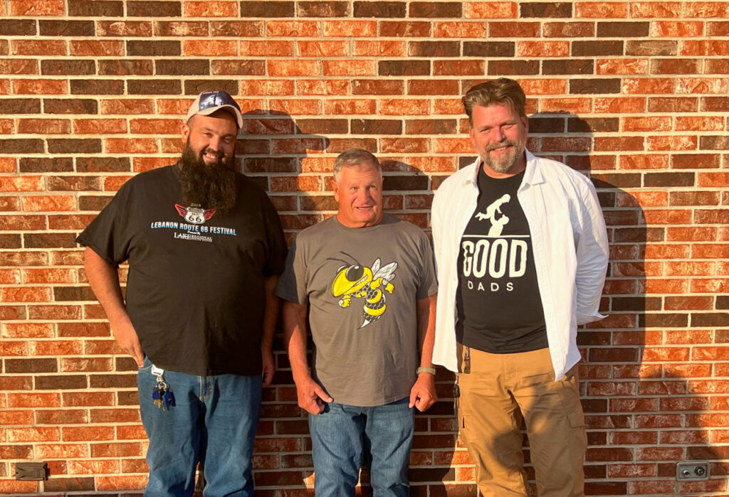 Facilitators Ross, Wayne and Matthew stand against a brick wall and smile for a group photo