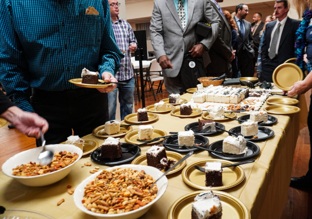 A line of guests forms at a table with a gold tablecloth and slices of cake with white frosting