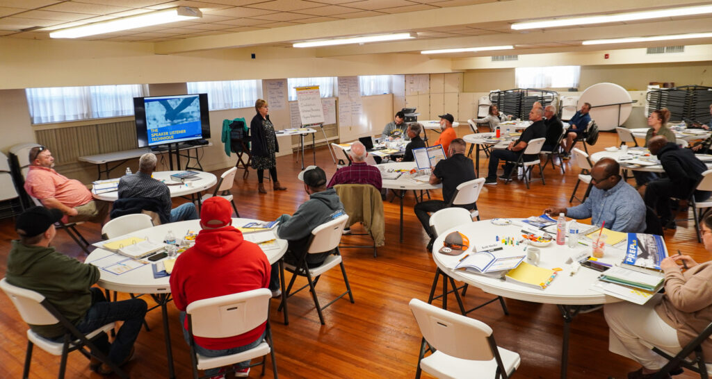 A wide shot of the classroom with participants looking at the front during conversation.