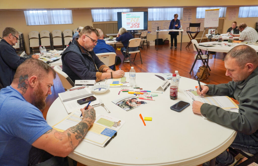 A group of three facilitators sit at a white table and write in their booklets.