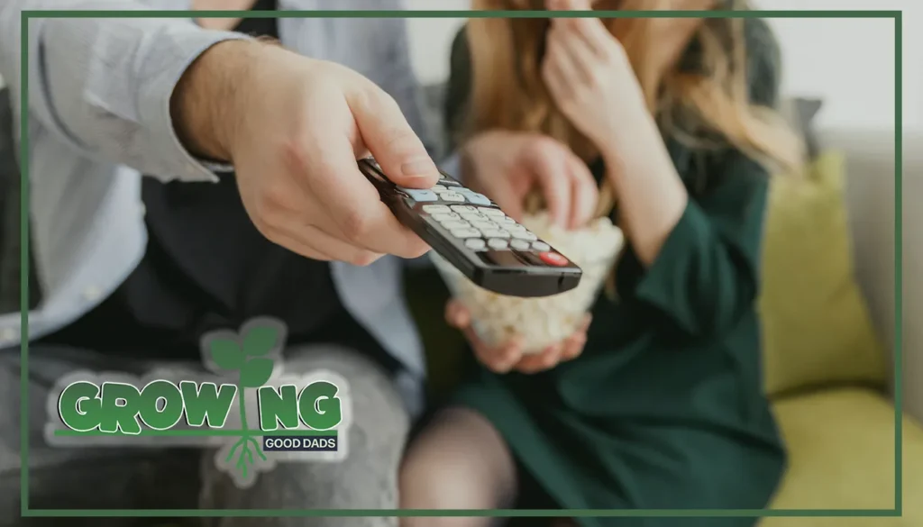 A man points a TV remote while a woman eats popcorn. Both are sitting together on a couch.