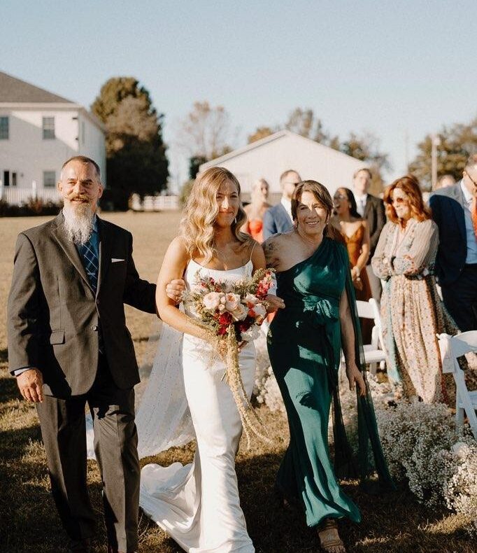 Gilbreth, wearing a suit, holds a hand against his daughter's back as he walks her down the aisle at her outdoor wedding.