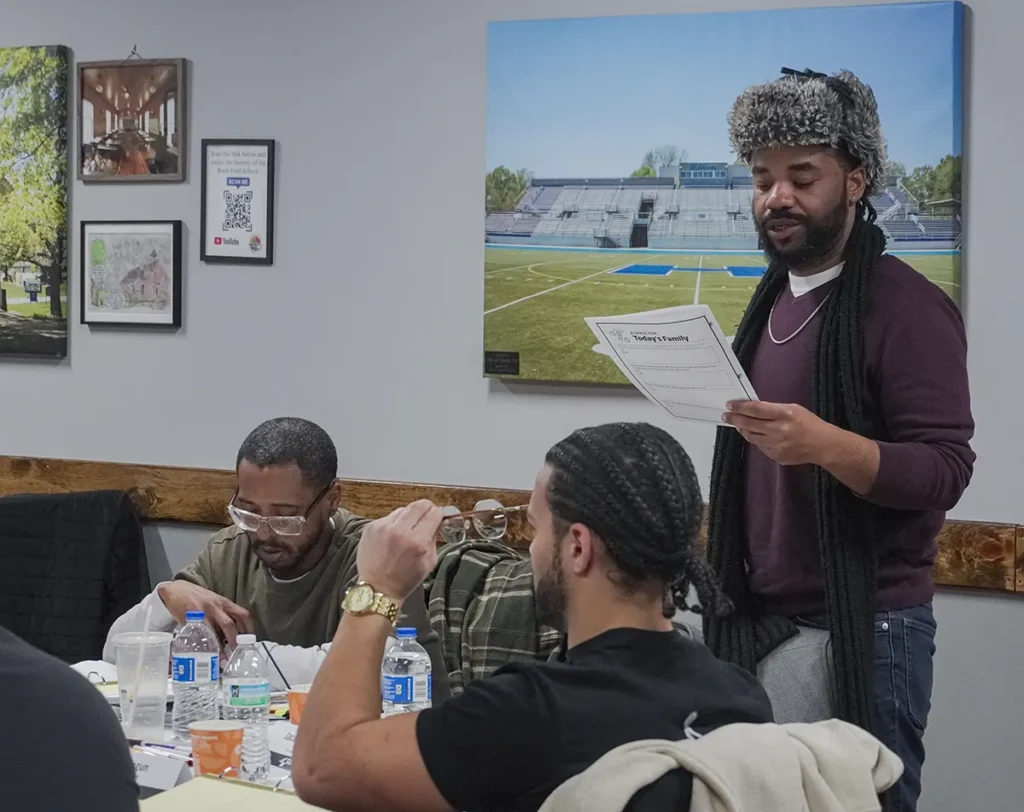 A man stands at his table and reads from his participant manual during training camp.