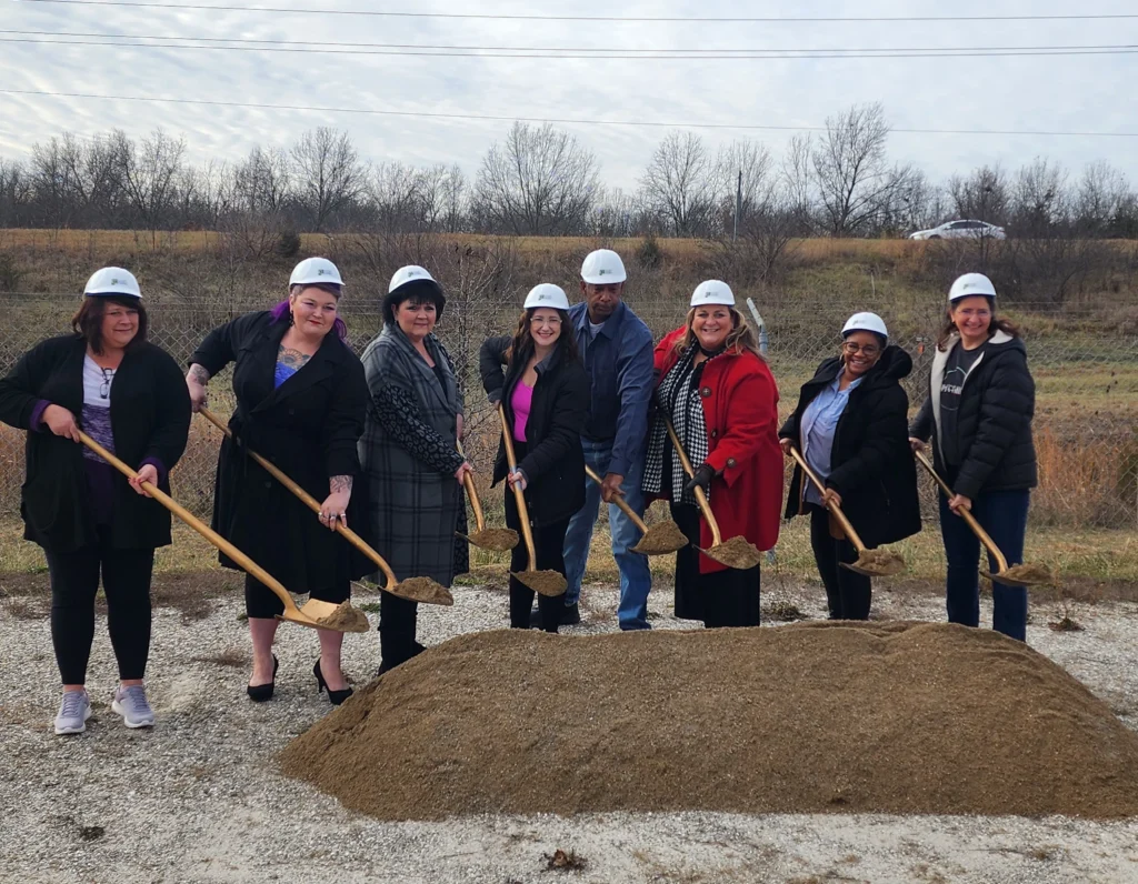 A group of people in hard hats holding shovels smile at a ground-breaking ceremony