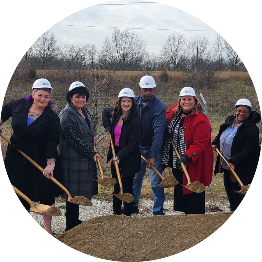 A group of people in hard hats holding shovels smile at a ground-breaking ceremony