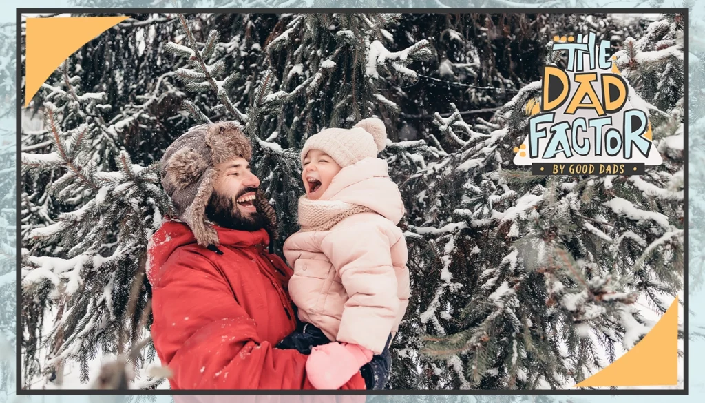 A father holds his young daughter. Both are bundled up outside in the snow.