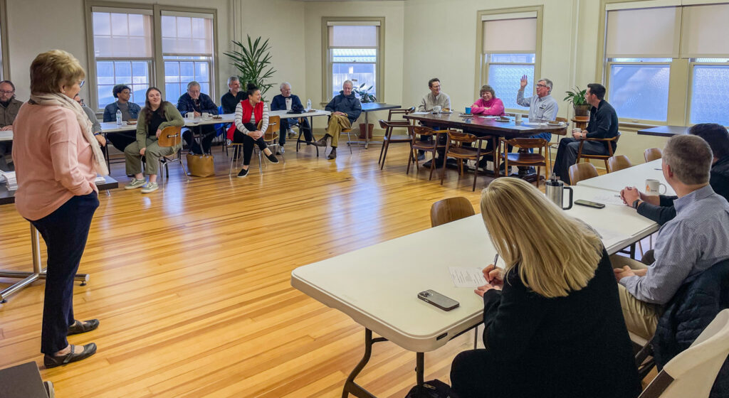 A group of participants sit at their tables while Dr. Jennifer L. Baker, founder and director of Good Dads, stands at the front of the room to give her presentation