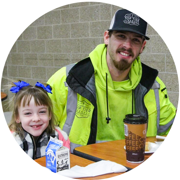 A dad and two daughters sit at a school lunch table to participate in a Good Dads Strong Schools activity