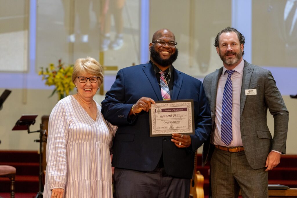 Graduate Kenneth Phillips receives his diploma with Dr. Jennifer L. Baker and board member Joshua Wemple.