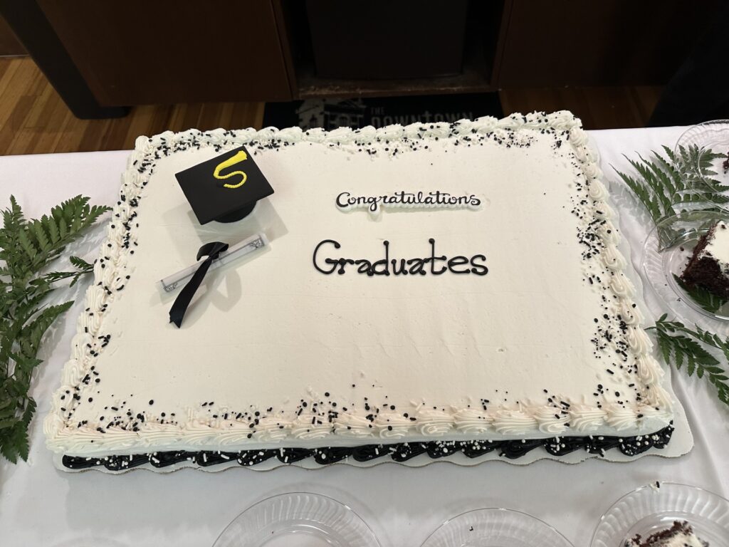 A cake with black and white icing decorated with a graduation cap and diploma. Words on the cake read "congratulations graduates"