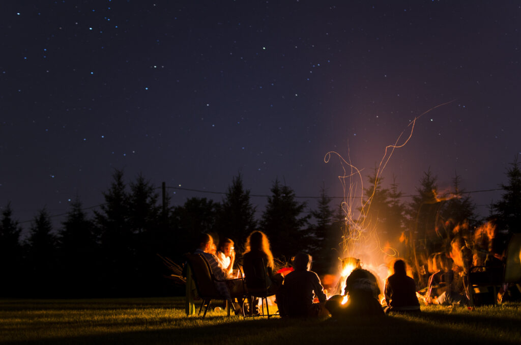 A nighttime image of a group of silhouetted people gathered around a bright campfire against a dark sky
