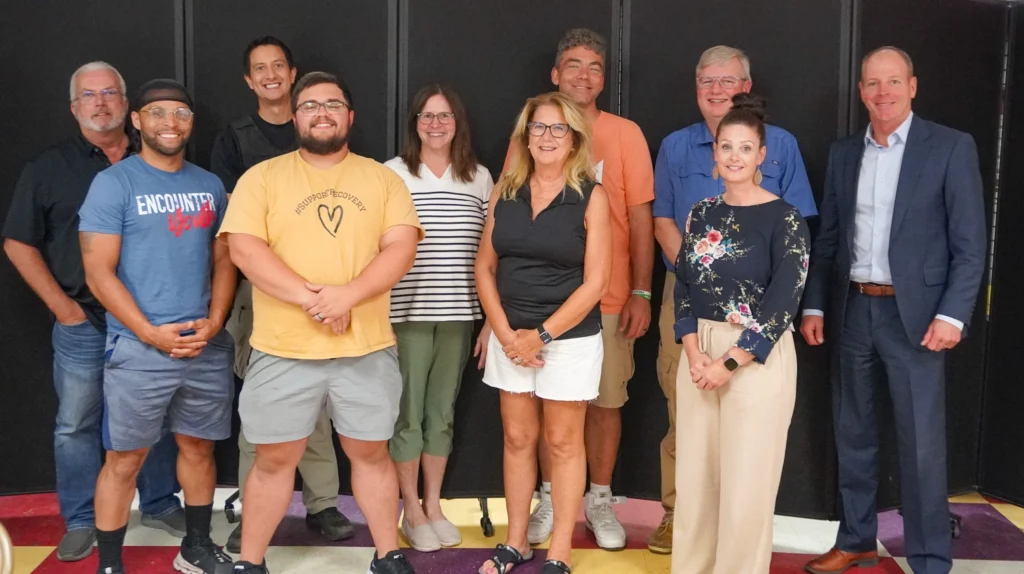 A group of people, members of the Good Dads Chillicothe Advisory Board, stand against a dark background for a group photo.