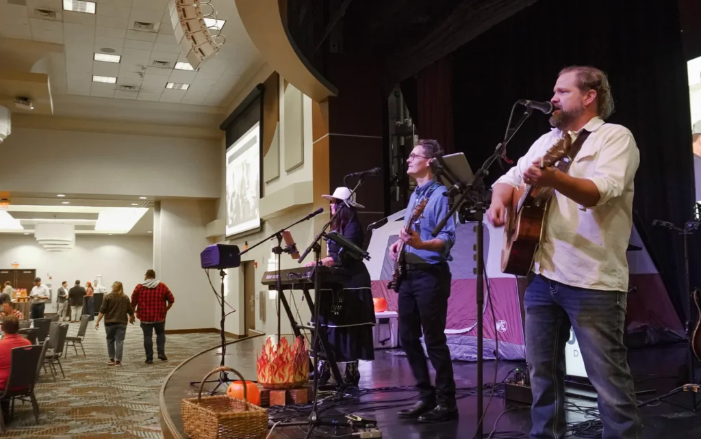 Members of the cover band Deja Crew play on keyboard, bass and acoustic guitar while standing on a stage and facing the audience