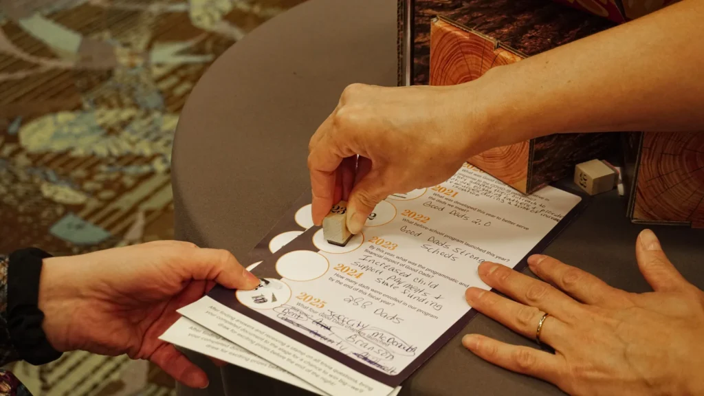 A Good Dads volunteer stamps the passport of a guest as she shares a piece of Good Dads history at her trivia station.
