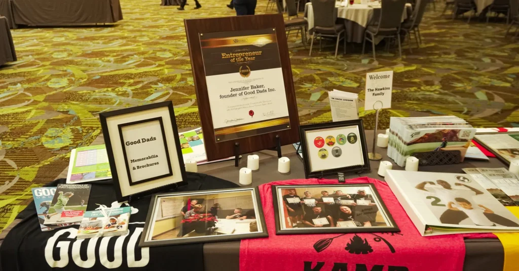 A memorabilia table at the fundraising dinner: a table with a gray tablecloth with brochures, framed photos, T-shirts, flyers and tealights strewn across it.