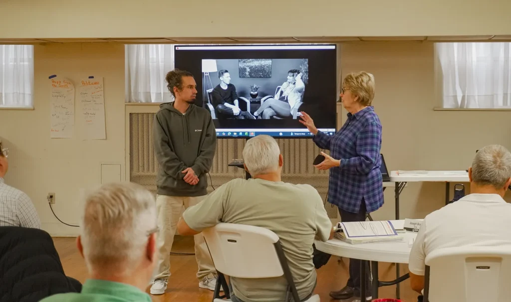 Good Dads founder and director Dr. Jennifer L. Baker stands at the front of the classroom with a volunteer to demonstrate a communication and listening exercise during the Good Dads 2.0 Training Camp in November 2025.