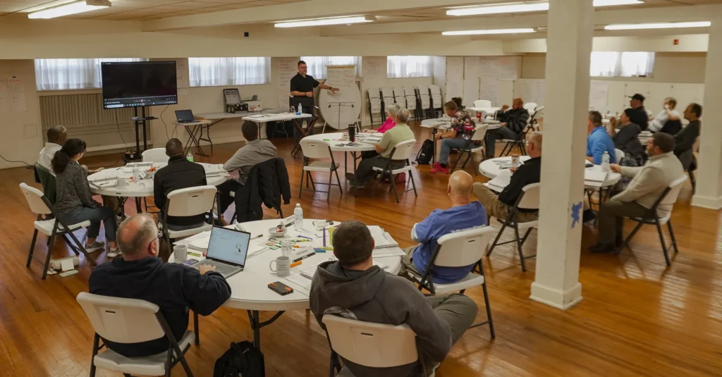 Good Dads master facilitator Matthew Johnson stands at the front of a large classroom at the Downtown Church in Springfield, MO, addressing a large group of Good Dads 2.0 facilitators during Training Camp.
