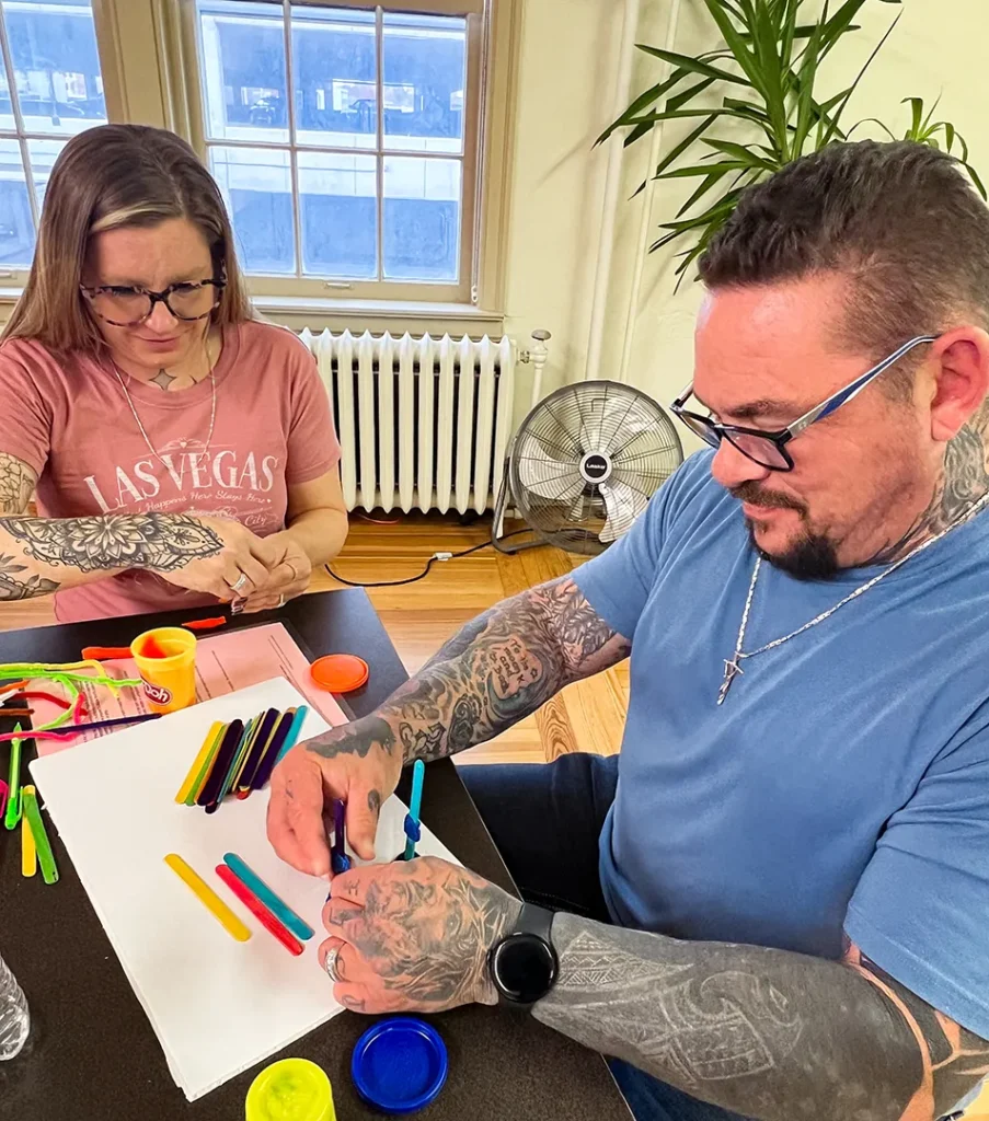 Two participants at Good Dads' training camp in November 2025, a man and a woman, sit next to each other and collaborate to make small Play-Doh and pipe cleaner sculptures to represent a healthy relationship as part of the Within My Reach curriculum training.
