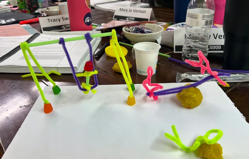 A close-up of a sculpture, resembling a playground swing-set and see-saw, made of pipe cleaners and Play-Doh.