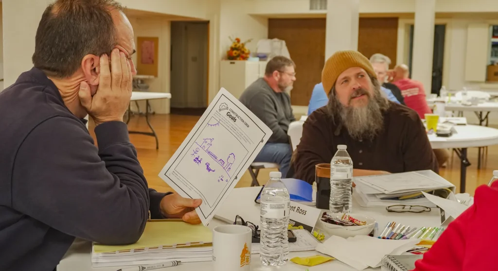 Three facilitators at Good Dads Training Camp in November 2025 sit at a round table and participate in a group discussion in a classroom space at the Downtown Church in Springfield, MO.