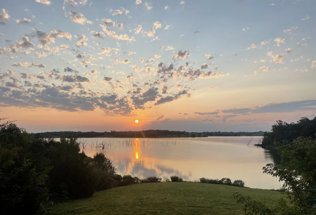 An expansive blue sky, dotted with clouds, during sunset, reflected over a serene pond.