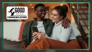 Good Dads Communicators: A man and woman sits together on a couch, smiling. The man is looking at the woman and smiling, his arm wrapped around her