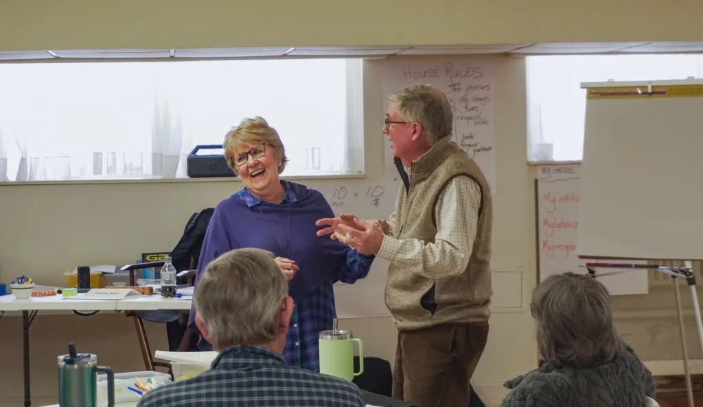 Good Dads founder and director Dr. Jennifer L. Baker laughs at her husband, Paul, as he jokes with the group at the front of the room during the January 2026 Good Dads Plus Us Training Camp in Springfield MO.