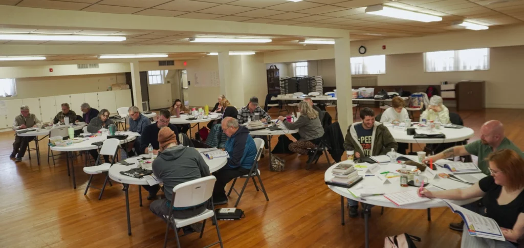 A wide-angle of the classroom, with facilitators collaborating at their tables, during the January 2026 Good Dads Plus Us Training Camp in Springfield MO.