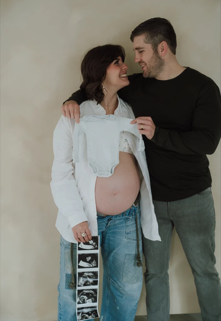Stan and Allie Adams hold each other while smiling at one another, with Allie's pregnancy belly exposed.
