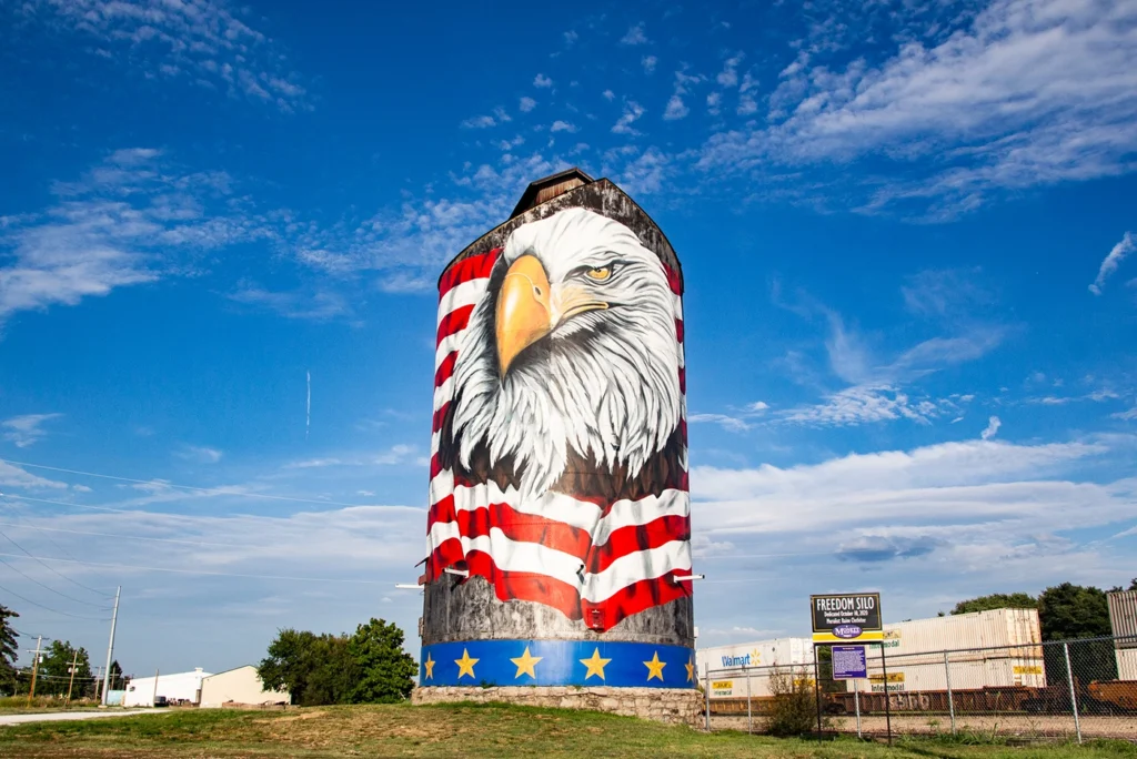 Freedom Silo, a tall grain silo in a green field painted with a giant, detailed head of a bald eagle in front of an American flag, at a park in Monett, MO.