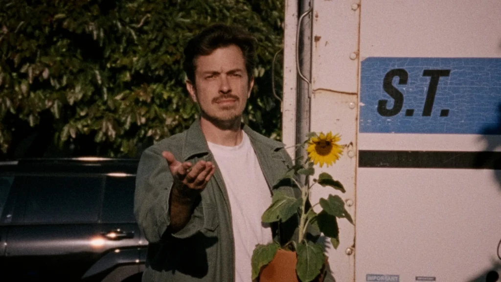 A father holds a sunflower, his other hand outstretched in the viewer's direction