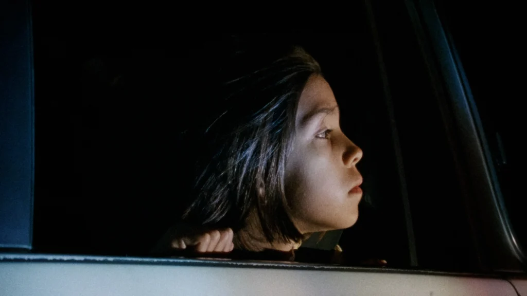 A pensive young girl looks out of a car window at night.