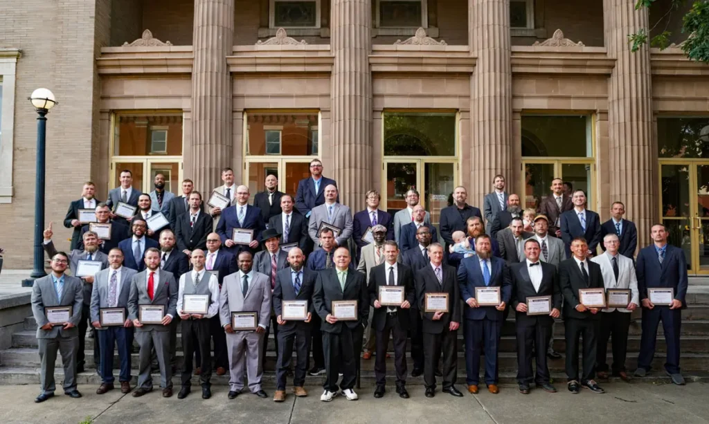 A group of 50 dads in suits line up for a group photo following Good Dads Graduation in June 2026.
