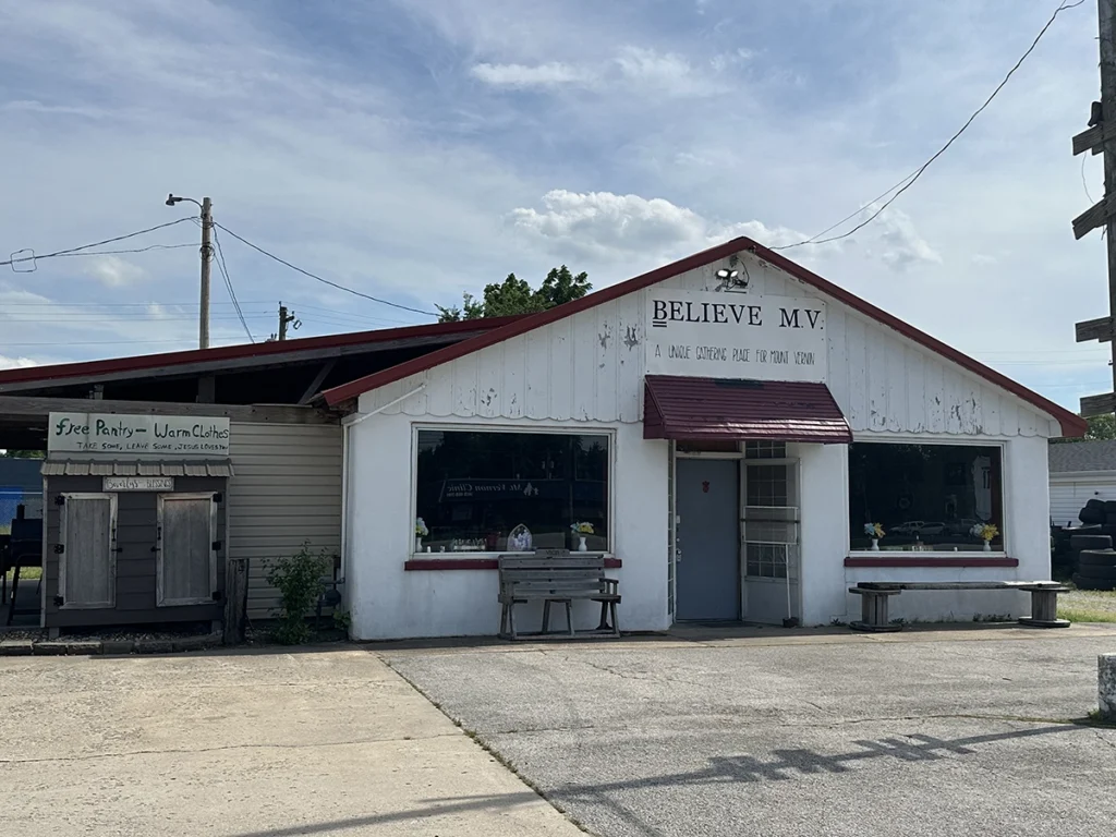 Exterior of a white building with a red roof: A sign at the front says Believe MV.