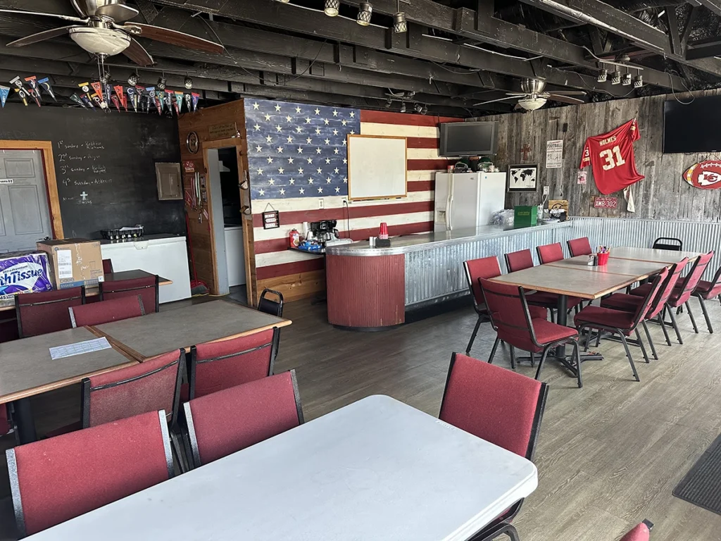 A room filled with tables and chairs, grey wooden walls and an accent wall with an American flag.