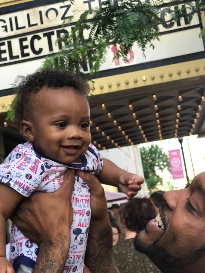 New Pathways graduate Ryan Washington hoists his young daughter above the sign of the Gillioz Theater