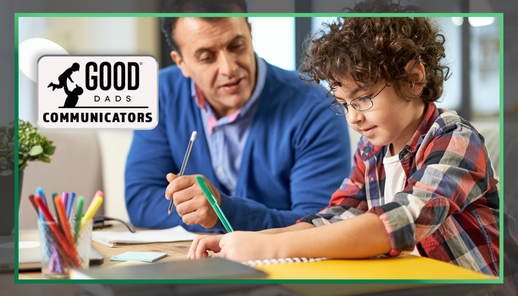 Good Dads Communicators: A father sits next to his school-aged son at a desk