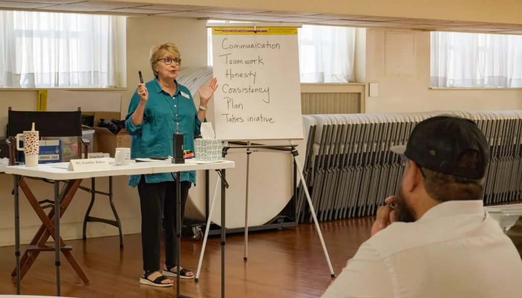 Good Dads' founder and executive director, Dr. Jennifer L. Baker, stands at the front of the class to write notes on a large piece of chart paper at the Downtown Church in September 2026 during Training Camp.