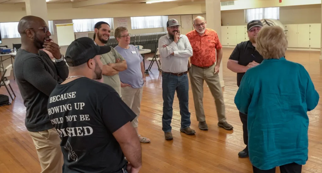 Good Dads' founder and executive director, Dr. Jennifer L. Baker, addresses a group of facilitators, who stand in a semi-circle, at the Downtown Church in September 2026 during Training Camp.