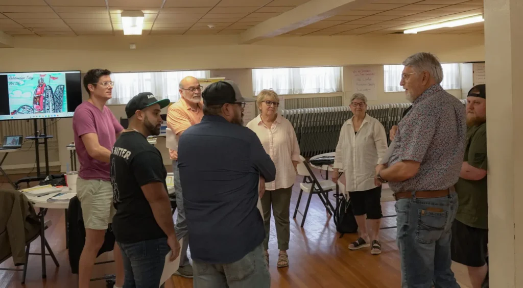 Good Dads facilitators stand in a circle in the classroom space and listen as they take turns explaining drawings they created as part of a relationships exercise during the September 2026 Good Dads Training Camp.
