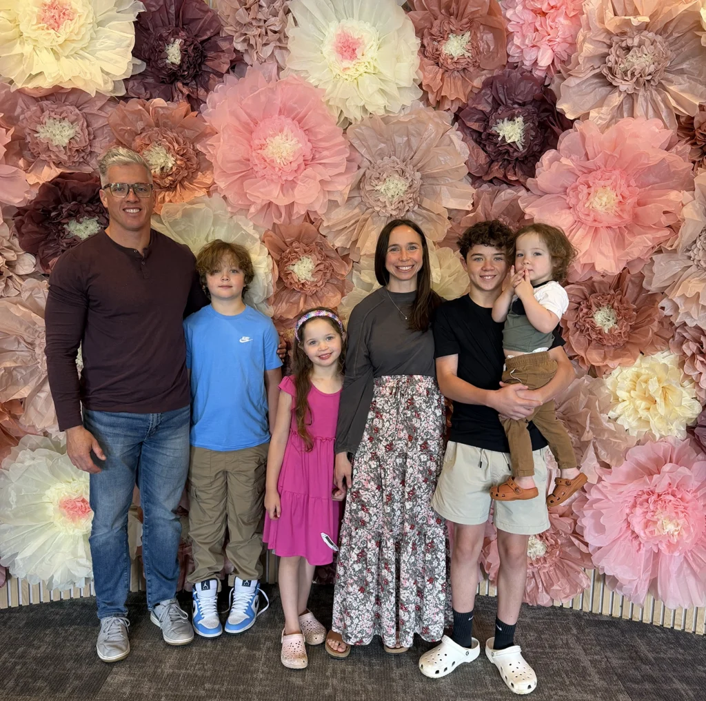 Dr. Luke Van Kirk, left, stands along a bright, decorative floral wall with his wife and four children.
